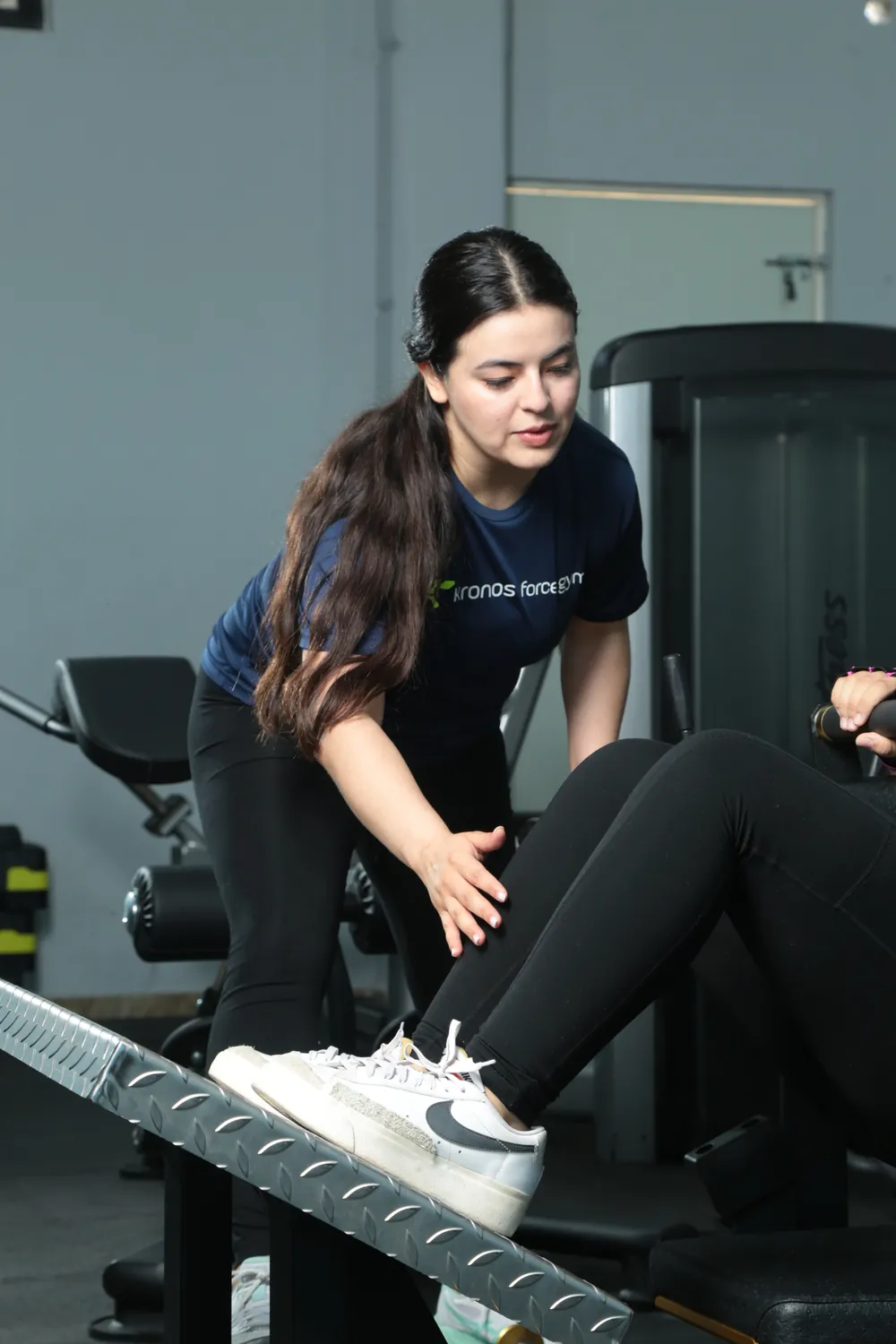 Socia ayudando a otra a acomodarse en la máquina de pierna